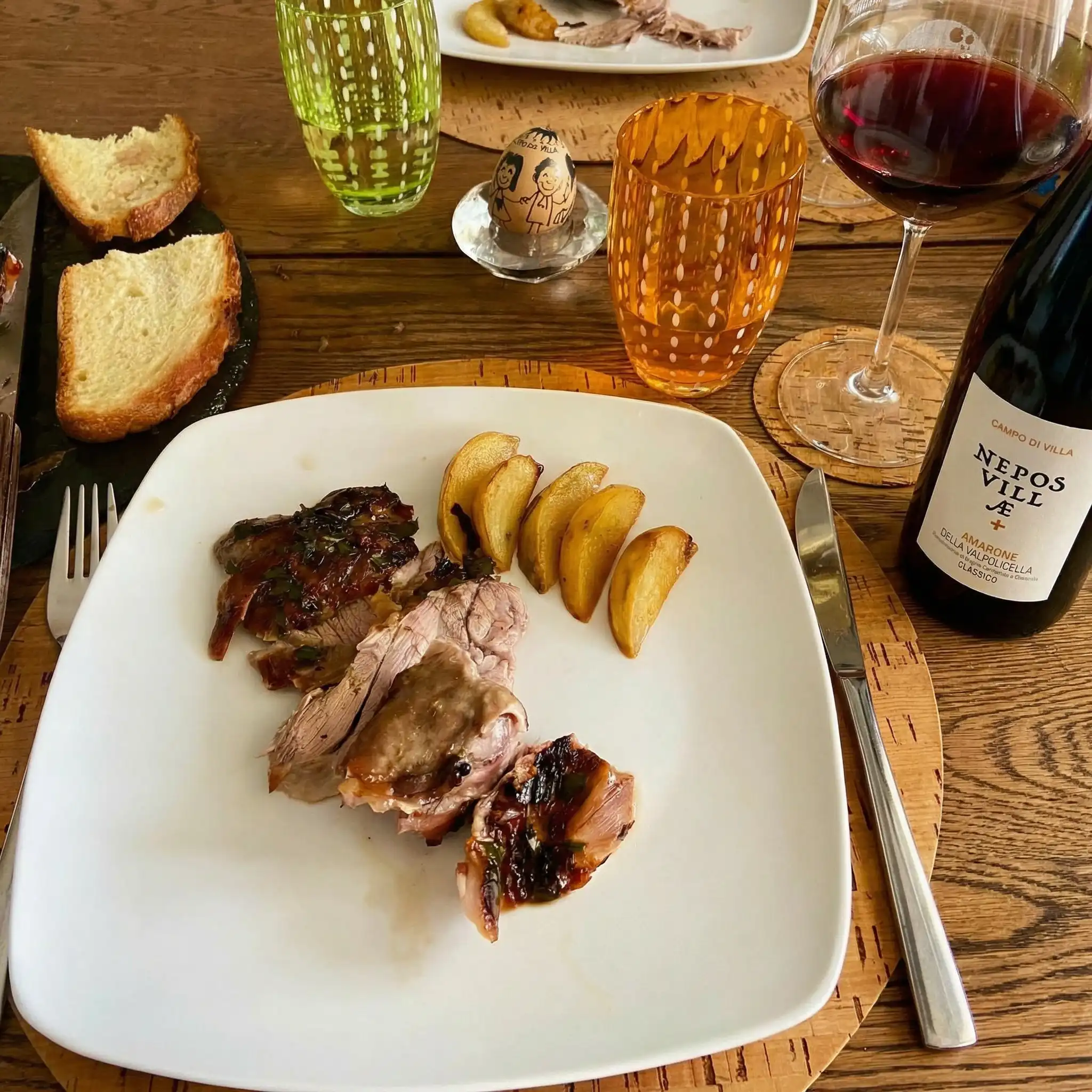 Roast lamb with golden potatoes, served on a plate at a set table with a bottle of red wine.
