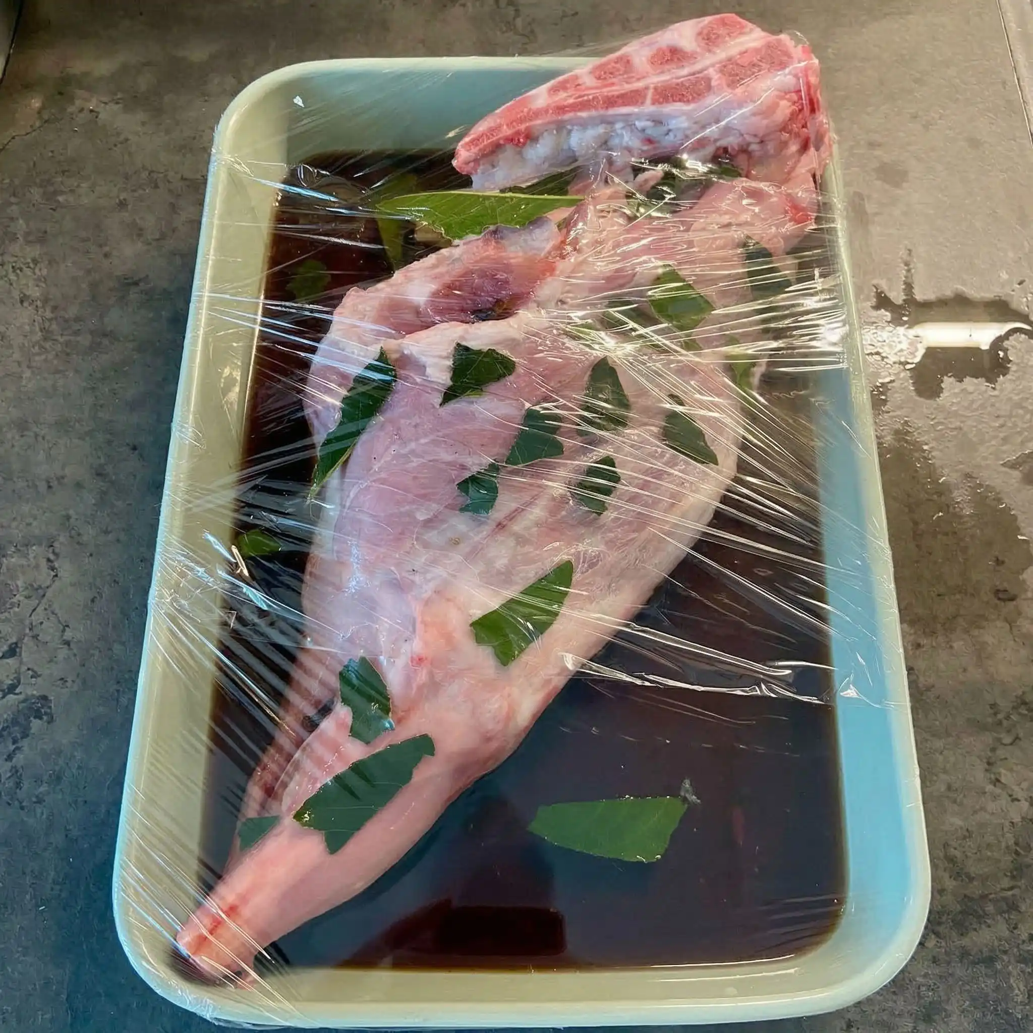 Agnello al forno con patate: agnello marinato nel vino rosso con erbe aromatiche in una ciotola.