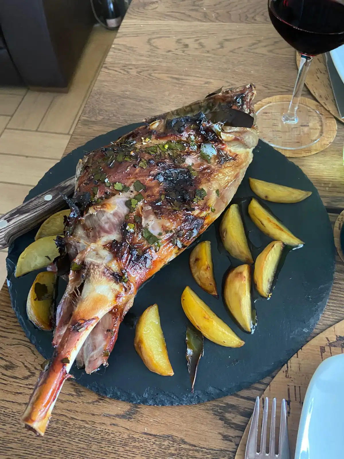 Agnello arrosto con patate dorate e calice di vino rosso su tavola apparecchiata, pronto per essere servito.